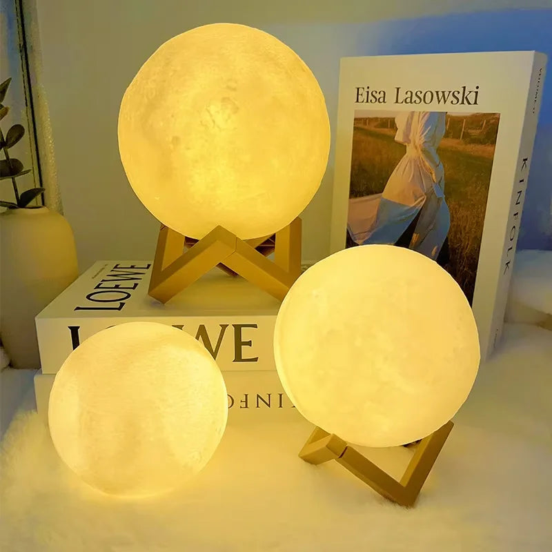 Three warm light moon lamps: two with wooden stands and one without stand, one lamp on a book, one on a table, and a book in the background