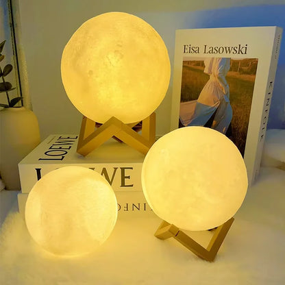 Three warm light moon lamps: two with wooden stands and one without stand, one lamp on a book, one on a table, and a book in the background